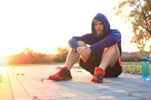 Handsome young man after run resting after jog at the park at sunset or sunrise. - 写真・画像