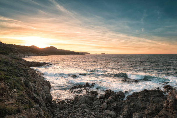 Coucher de soleil sur la côte rocheuse de la Balagne Corse avec mer agitée, ciel dratique et Ile Rousse au loin
 - Photo, image