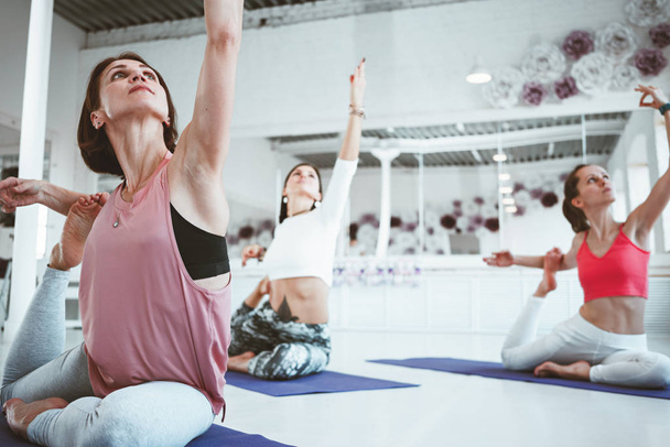 Strong fit woman training yoga poses on fitness mat together with group of people on background. Healthe care and lifestyle. - 写真・画像