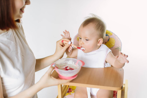 Mother Feeding Baby Sitting In High Chair At Mealtime - Valokuva, kuva
