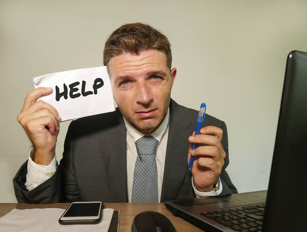 young depressed and frustrated businessman working in stress at office computer desk holding notepad asking for help feeling upset and overworked in corporate job problem and business crisis - Photo, Image