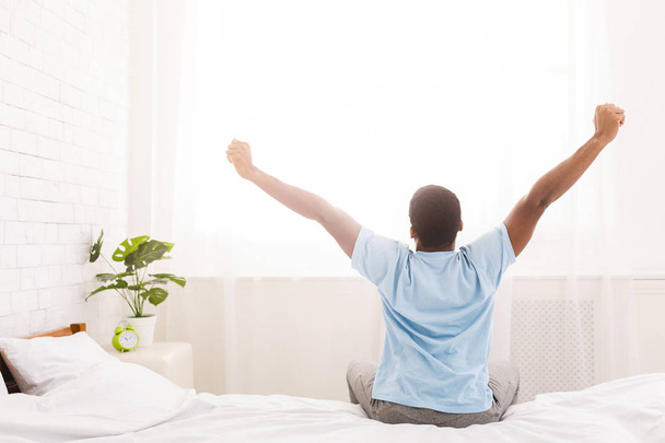 νεαρός άνδρας waking πάνω στο κρεβάτι και απλώνεται τα χέρια του - Φωτογραφία, εικόνα
