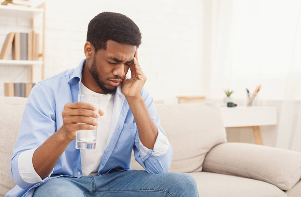 Afrikanisch-amerikanischer Mann mit Kopfschmerzen nimmt Tablette zu Hause ein - Foto, Bild