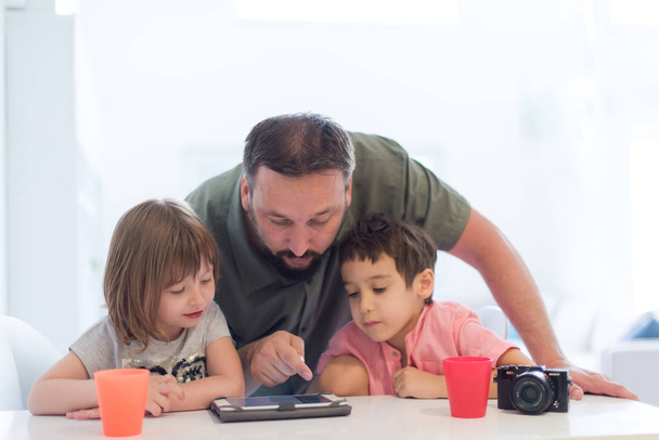 single father at home with two kids playing games and giving education lessons on tablet  computer at modern home - Foto, Bild