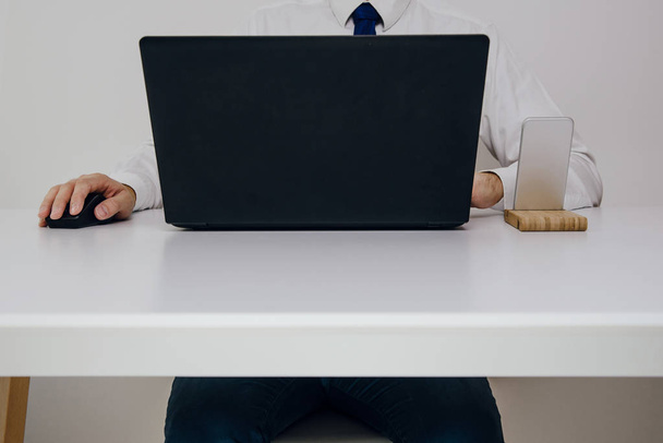 Trabajo de oficina. Un hombre está sentado frente a un portátil y está trabajando. Vista frontal de un empresario trabajador vestido con una corbata azul
. - Foto, Imagen
