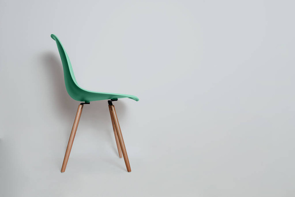 Een moderne groene retro stoel op een grijze, lichte pastel achtergrond. Zijaanzicht van een groene bureaustoel op houten poten. Het concept van moderniteit en ontwerp. - Foto, afbeelding