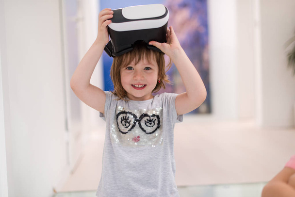 little gir at home wearing vr glasses putting hands up and playing games - Foto, Bild