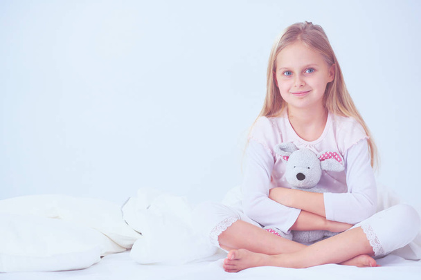 Little girl in the bedroom is sitting on the bed. Little girl is wearing a pajamas and sitting in bed . - Foto, Bild