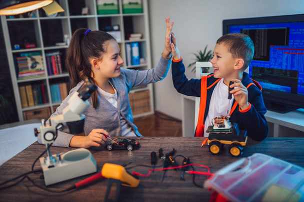 Happy smiling boy and girl constructs technical toy and make robot. Technical toy on table full of details - Photo, Image