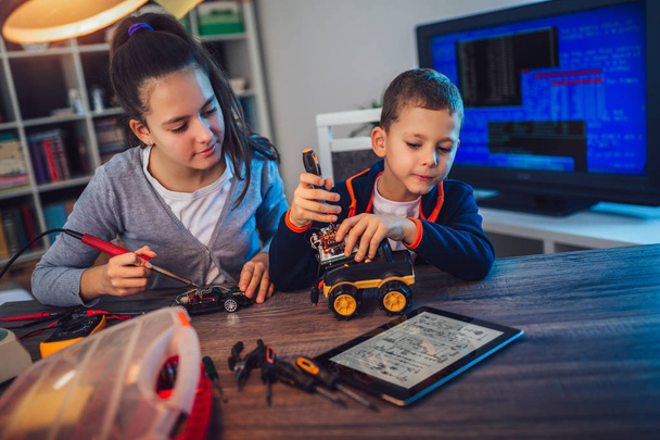 Щасливий усміхнений хлопчик і дівчинка створюють технічну іграшку і роблять робота. Технічна іграшка на столі повна деталей
 - Фото, зображення
