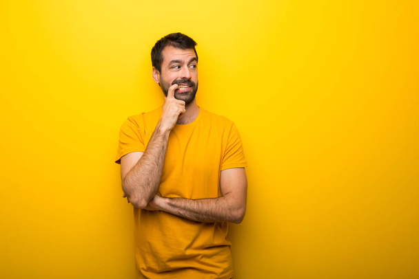 Homem na cor amarela vibrante isolado com dúvidas ao olhar para cima
 - Foto, Imagem