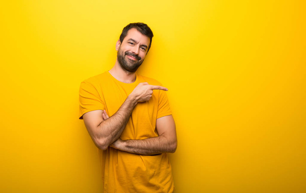 Man on isolated vibrant yellow color pointing finger to the side in lateral position - Photo, Image