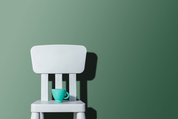 Blauw pastel stoel op een pastel achtergrond. Pastel kleuren. Groen pastel cup op de stoel. Kinderstoel van de blauwe kleur. Het concept van wachtkamers, verwachtingen, lifestyle. - Foto, afbeelding