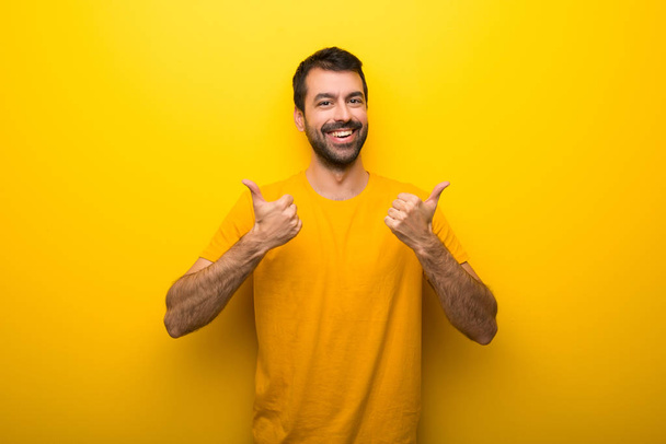 Man on isolated vibrant yellow color giving a thumbs up gesture with both hands and smiling - Photo, Image