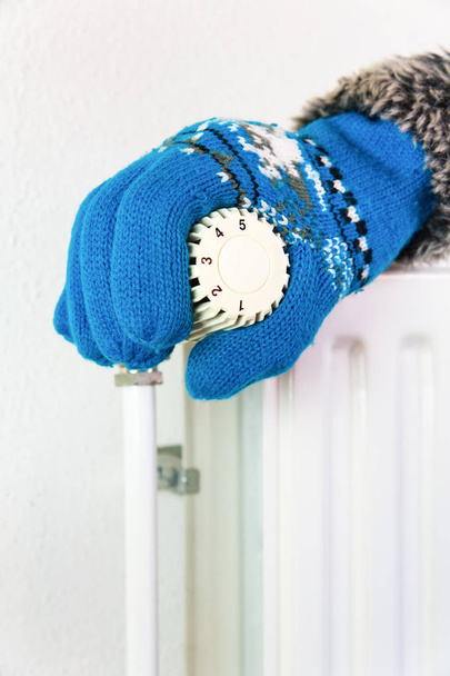 Mão vestindo luva transformando válvula de aquecimento no inverno frio
 - Foto, Imagem