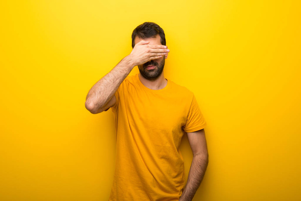 Man on isolated vibrant yellow color covering eyes by hands. Do not want to see something - Foto, afbeelding