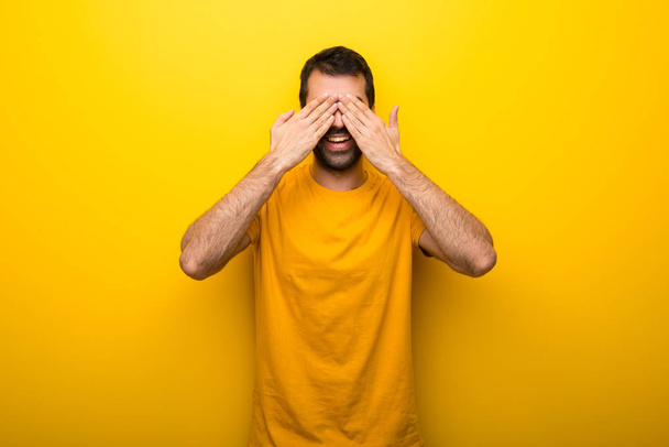 Чоловік на ізольованому яскраво-жовтому кольорі покриває очі руками. Здивований, щоб побачити, що попереду
 - Фото, зображення