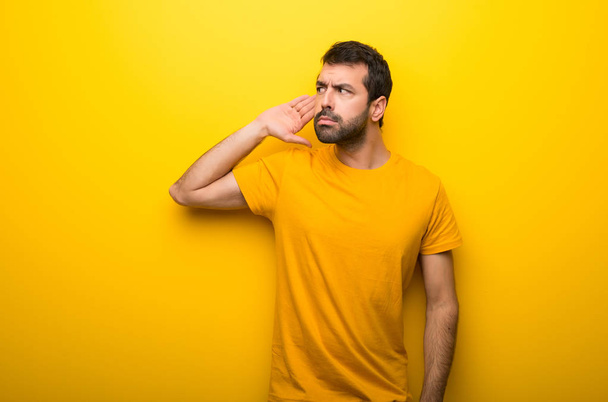 Man on isolated vibrant yellow color listening to something by putting hand on the ear - Photo, Image