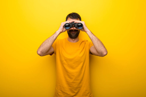 Man op geïsoleerde levendige gele kleur en op zoek naar iets in de verte met verrekijker - Foto, afbeelding