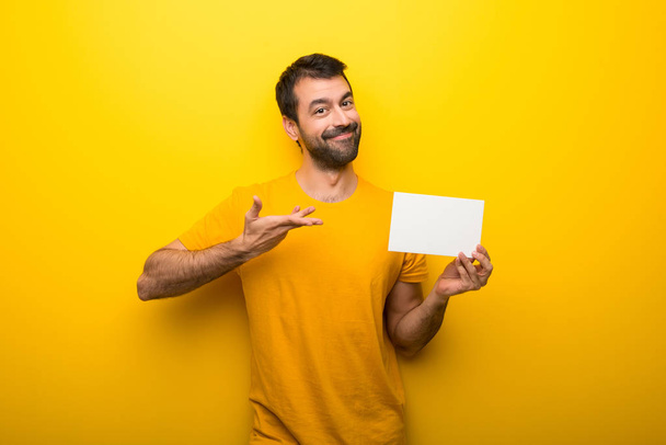 Man on isolated vibrant yellow color holding an empty white placard for insert a concept - Zdjęcie, obraz
