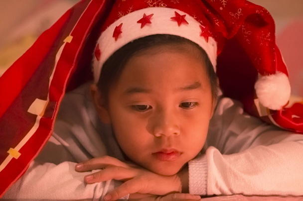 Menino usava um chapéu de Natal debaixo de um cobertor, triste e sozinho no quarto em uma noite fria de Natal
. - Foto, Imagem