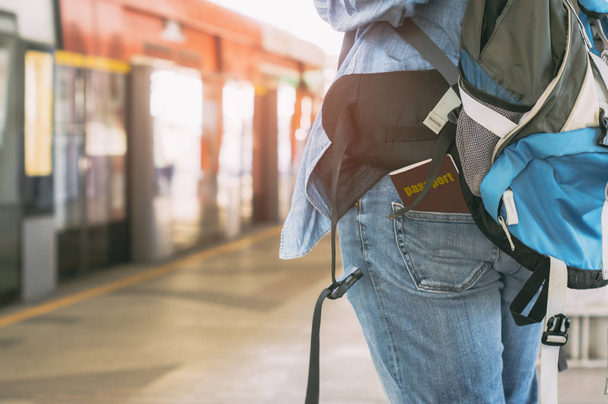 Οπίσθια όψη της ένα backpacker που περιμένουν για ένα τρένο με ένα διαβατήριο συνδεδεμένο με τζιν, με την έννοια του ελεύθερου χρόνου, planner περιπέτεια και τα ταξίδια με το τρένο, κατά τις καλοκαιρινές διακοπές από τον εαυτό σας. - Φωτογραφία, εικόνα