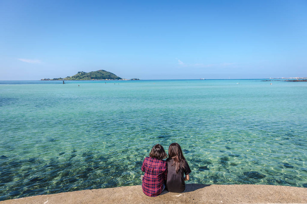 Две молодые девушки наслаждаются удивительным синим акварельным морем Чеджу в Южной Корее
 - Фото, изображение