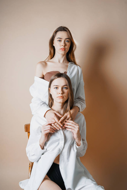 ファッション モデル 2 つの双子の姉妹がベージュ色の背景に分離されたカメラを見て美しい裸の女の子  - 写真・画像