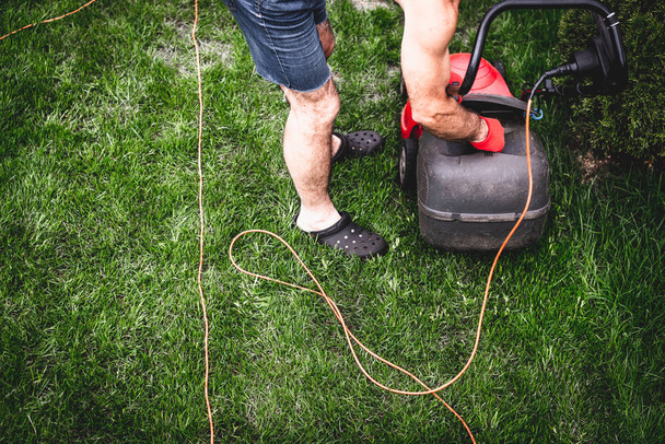 Top view on mowing the grass. The gardener mows the grass with a red electric mower. Work in the garden, spring cleaning. Care for the garden and grass. - Photo, Image