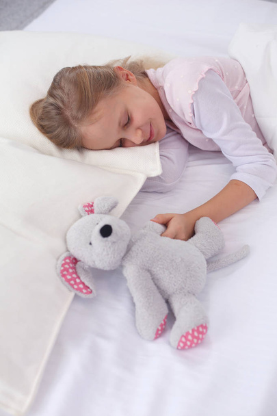 Lapsi pieni tyttö nukkuu sängyssä lelu nallekarhu
. - Valokuva, kuva