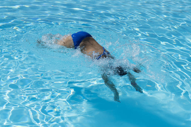 Жінка занурюється у басейн. Молода красива дівчина плаває в басейні. Брюнетка розслабляється в чистій теплій воді в сонячний день. Вид зверху Крупним планом Повільний рух
 - Фото, зображення