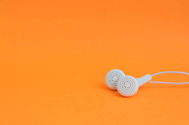 White modern earphones lies on a bright orange background. - Foto, Bild