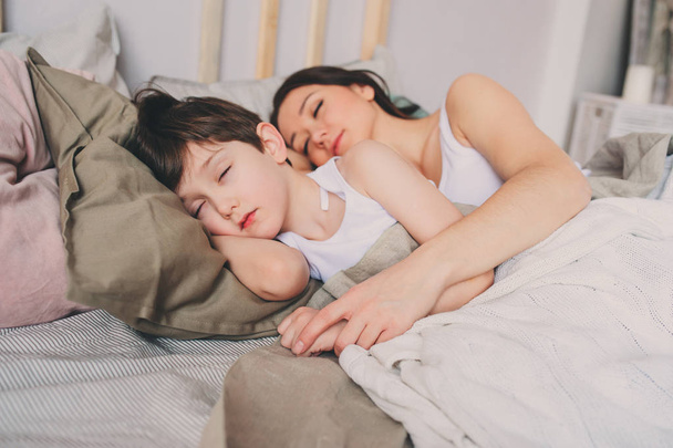 mother and child son sleeping together in bed, waking up in the morning or going to sleep - Фото, изображение