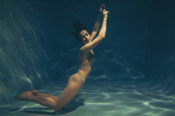 cute sporty girl swims underwater as a free diver in sheer jumpsuit alone - Fotó, kép