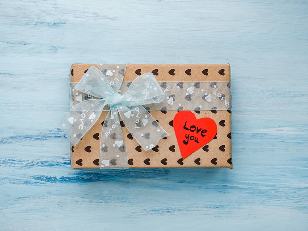 Box with a gift, tied with a ribbon, note with sweet words of love and tinsel in the shape of hearts. Close-up, flat lay, isolated. Congratulations for loved ones, relatives, friends and colleagues - Фото, изображение