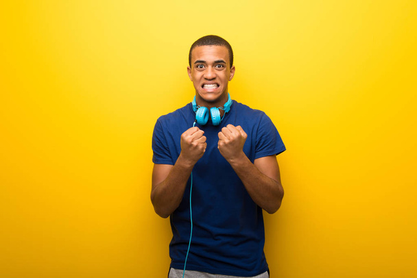 African american man met blauw t-shirt op gele achtergrond gefrustreerd door een slechte situatie - Foto, afbeelding