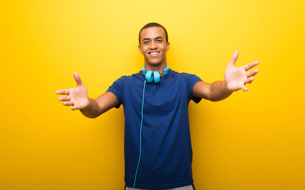 Африканский американец в синей футболке на желтом фоне представляет и приглашает прийти с рукой
 - Фото, изображение