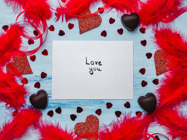 Note with sweet words of love, ribbons, colorful feathers, candy and tinsel in the shape of a heart. Top view, isolated background. Congratulations for loved ones, relatives, friends and colleagues - Foto, Bild