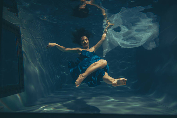 милая спортивная женщина плавает под водой как свободный ныряльщик в синем вечернем платье в одиночку
 - Фото, изображение