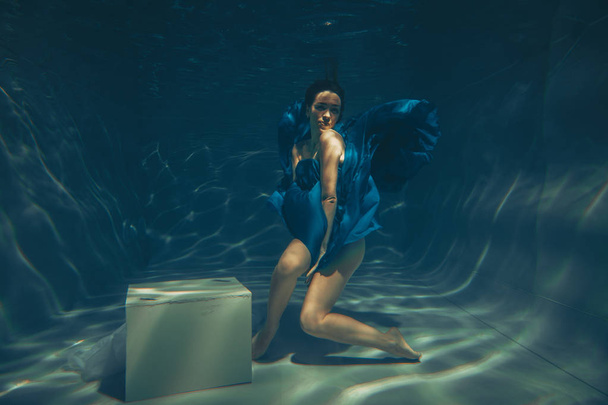 elegant pretty woman swims underwater like a free diver in a blue evening dress alone - Photo, Image