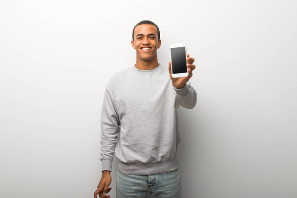 African american człowieka na tle białej ściany patrząc na kamery i uśmiechając się podczas korzystania z telefonu komórkowego - Zdjęcie, obraz