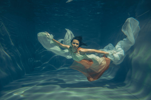 элегантная стройная девушка плавает под водой, как свободный дайвер в белом вечернем платье с красивой тканью
 - Фото, изображение