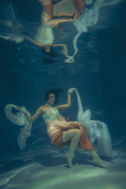 elegante chica delgada nada bajo el agua como un buzo libre en un vestido de noche blanco con tela hermosa
 - Foto, Imagen