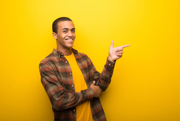 Młody człowiek african american na żółte tło wibrujący palcem wskazującym na bok w pozycji bocznej - Zdjęcie, obraz