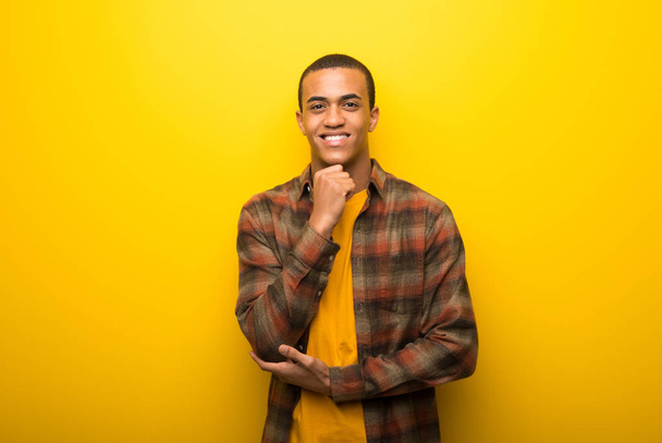 Νεαρός αφρικανική αμερικανική άνθρωπος σε ζωντανό κίτρινο φόντο χαμογελώντας και κοιτάζοντας προς τα εμπρός με αυτοπεποίθηση πρόσωπο - Φωτογραφία, εικόνα
