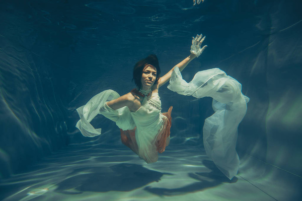 elegante chica delgada nada bajo el agua como un buzo libre en un vestido de noche blanco con tela hermosa
 - Foto, imagen