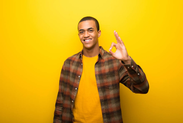 Молодий афроамериканець людиною на яскраві жовтому тлі показ ОК знак пальцями - Фото, зображення