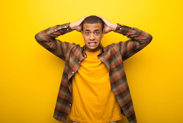 Giovane uomo africano americano su sfondo giallo vibrante prende le mani sulla testa perché ha l'emicrania
 - Foto, immagini