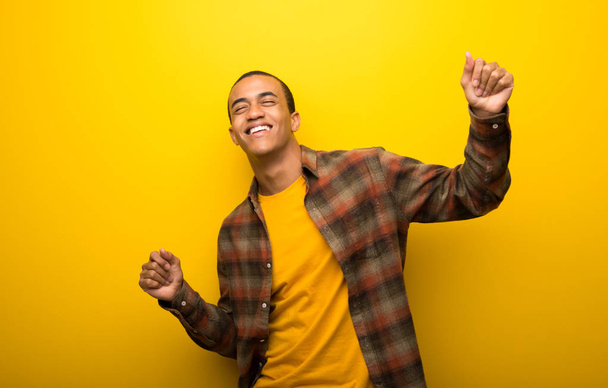 Νεαρός αφρικανική αμερικανική άνθρωπος σε ζωντανό κίτρινο φόντο απολαύσετε χορό ενώ ακούτε μουσική σε ένα πάρτι - Φωτογραφία, εικόνα