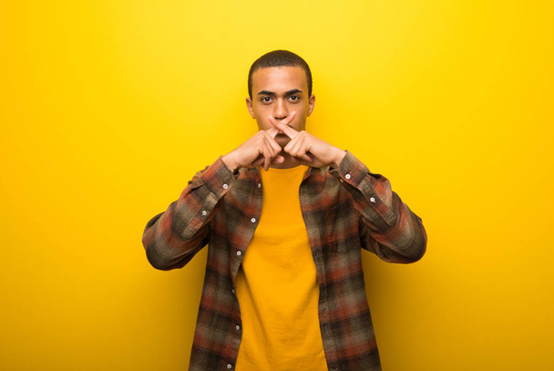 Jeune homme afro-américain sur fond jaune vif montrant un signe de silence geste
 - Photo, image